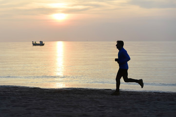 Fototapeta premium silhouette young sport man running outdoors on beach at sunset with orange sky