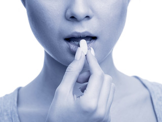 Woman taking a tablet. Close up hand with a pill and the mouth. Toned image, isolated on white...
