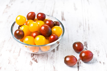 Brown and yellow fresh cherry tomatoes with water drops in glass bowl on white wooden table