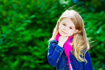 Outdoor portrait of beautiful blond little girl with long hair wearing blue jeans jacket and pink scarf