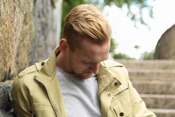 An attractive man standing, leaning against a stone wall wearing a yellow jacket outside on a sunny...