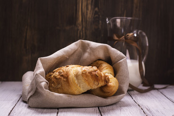 Fresh almond croissants and glass jar of milk. Rustic style. Toned image. Selective focus