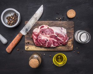 raw pork steak with herbs, oil knife for meat on a cutting board on wooden rustic background top view close up