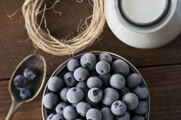 Photo of a frozen blueberrys in metal mug and bottle of milk standing on old wooden table.