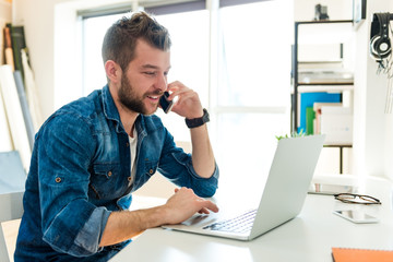 Young hipster  businessman working on laptop and talking on mobile phone