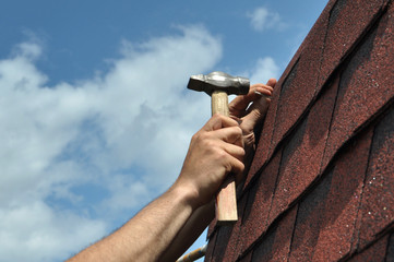 Hand with a hammer to drive a nail, roof repairs