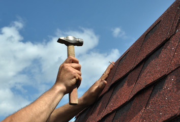 Hand with a hammer to drive a nail, roof repairs