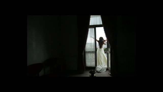 Beautiful bride with long dark hair having fun on the balcony with high windows with dark apartments on the background