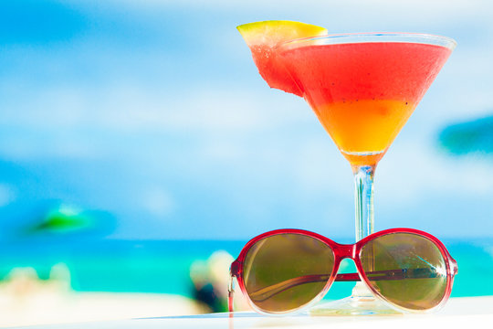 picture of fresh red and yellow cocktail with sunglasses near tropical