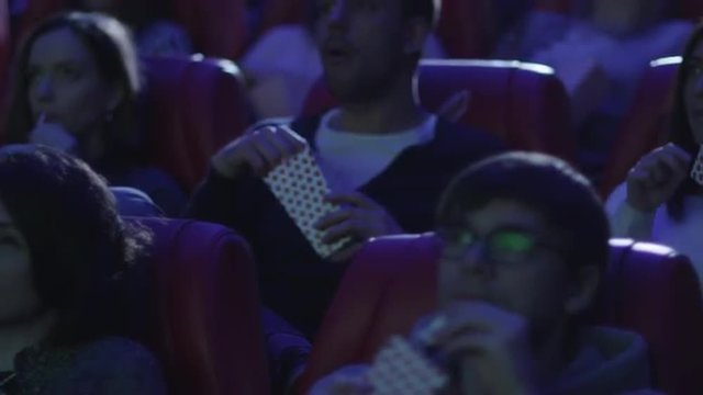 Group of people are eating popcorn while watching a film screening in a movie cinema theater. Shot on RED Cinema Camera.