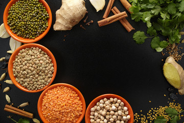 Bowls with legumes and indian spices, fresh and dried on black b