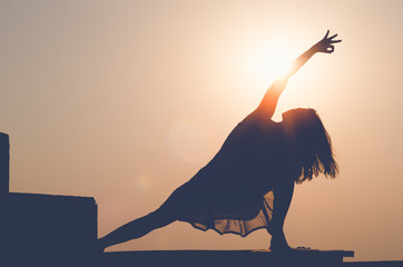 Beautiful woman doing a yoga exercise on the rooftop of a skyscraper at sunset