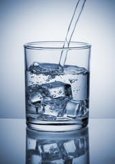 Water pouring into glass with ice cubes