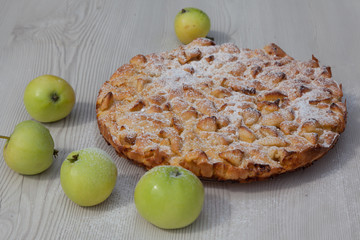 Apple pie iced with sugar on a white wooden table, fresh green and yellow apples