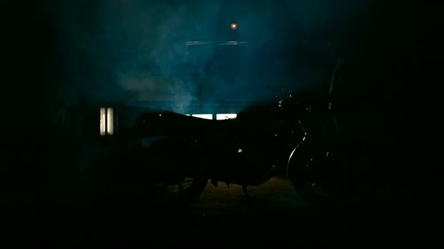 Silhouette of young male biker rolls a motorbike into garage. 
4K 60 FPS slow motion shot