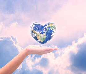 World in heart shape with over women human hands on blurred natu