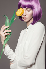 Portrait of beautiful girl with purple hair and yellow tulips in the studio on a gray background, the concept of health and beauty