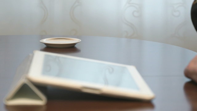 Woman works over documents using a digital tablet and drinks coffee