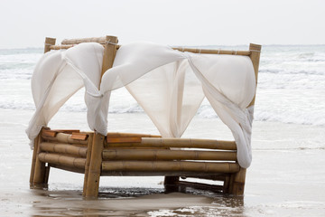 lit en bambou sur une plage avec des voiles blanches