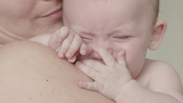 caucasian baby boy crying on mum's shoulder close up slow motion