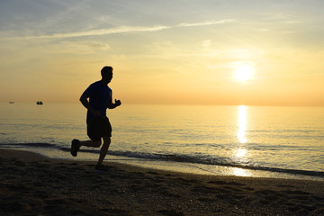 silhouette young sport man running outdoors on beach at sunset with orange sky