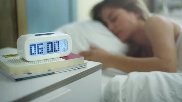 Young woman is sleeping in the morning when ring the alarm. She switch off it and continue sleeping