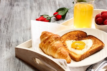 Breakfast in bed with heart shaped egg in basket croissant and juice
