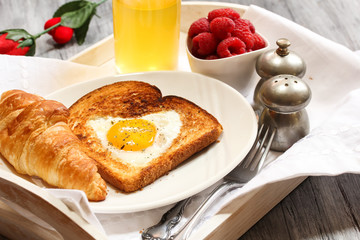 Breakfast in bed with heart shaped egg in basket croissant and juice