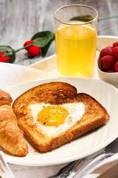 Breakfast in bed with heart shaped egg in basket croissant and juice