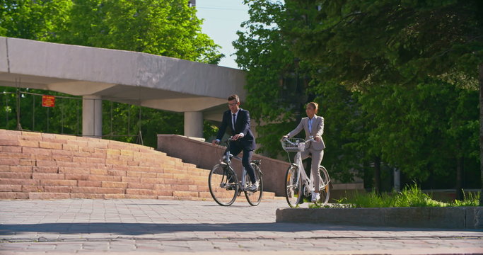 Tracking shot of Asian office workers riding their bikes to work and talking on the move   