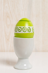 White ceramic egg cup with a green hand painted easter egg in front of a wooden background