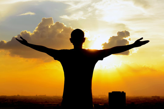 Silhouette of a man raising his arms on  twilight sky background
