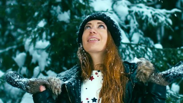 120 FPS Slow motion close up shot of young Caucasian girl standing under the falling snow in a winter forest