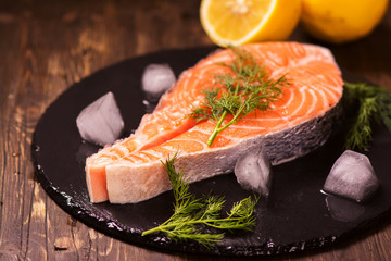Raw salmon steak with lemon and herbs over wooden background. Healthy food or diet concept. Selective focus
