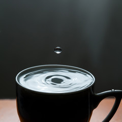 Blue water drop and black mug, dark background. copy space