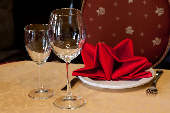 Table in a restaurant with a tablecloth, red napkins, wine glasses and cutlery.