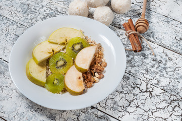 Oatmeal with apples, pears, walnuts and kiwi in a white bowl. Top view