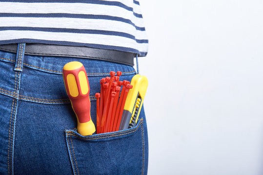 Tools for electrician in back pocket of blue jeans worn by a woman. Screwdriver, sharp knife and zip ties.
