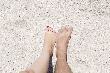 Couple's feet in the sand. White sand beach.
