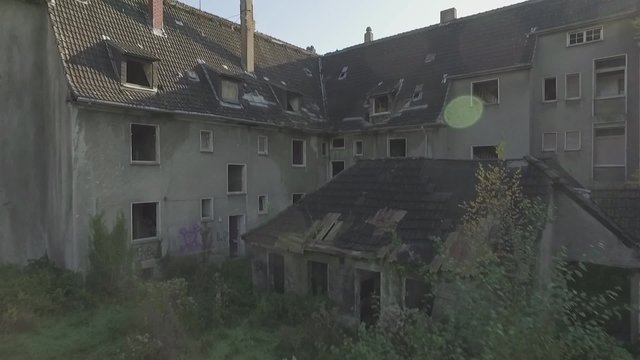 Aerial of an abandoned quarter in the coal-mining town Gladbeck, Germany, slow ascent forward over shabby row of houses, house top and chimney ending on residential area. flat s-log colour profile.
