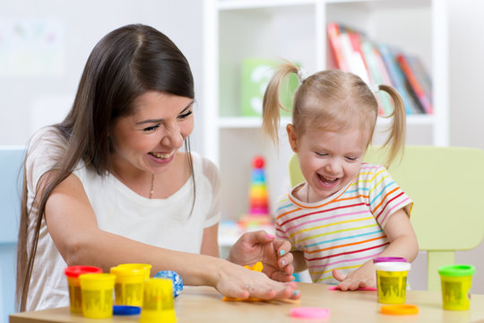 Young pretty woman and child girl playing with colorful clay in nursery