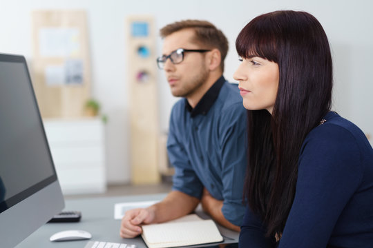 nachdenkliche kollegen sitzen am schreibtisch und schauen auf den pc