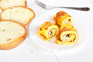 Rolls of omelette with cheese on a plate on white wooden background
