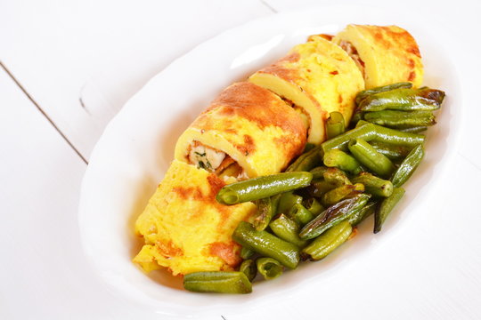 Rolls of omelette with cheese on a plate on white wooden background
