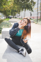 Young caucasian reddish hair woman sitting on a small wall, smok