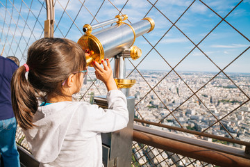 Naklejka premium Little girl using the telescope in the Eiffel Tower