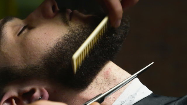 Barber cuts the beard hair of the client with scissors slow motion close up