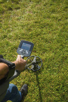 A man's arm holding a metal detector just about ground level, searching for metal objects under the ground. 