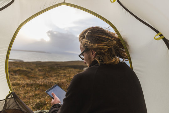 Man sitting in tent and using digital tablet