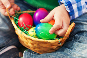 Fototapeta na wymiar Small basket with colorful easter eggs in baby's hands